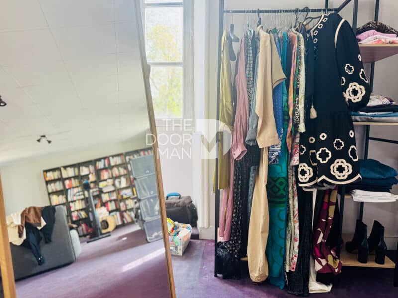 Interior of a house with clothes hanging up and a bookcase in the background.