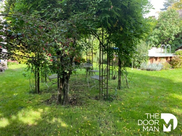 Jardin d'une maison bourgeoise avec une structure en fer forgé et des chaises, Montfort-l'Amaury.
