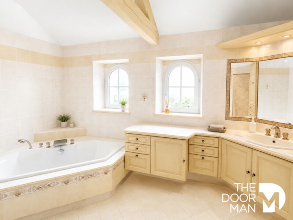 Salle de bain spacieuse avec baignoire et meuble en bois clair, fenêtres arrondies.