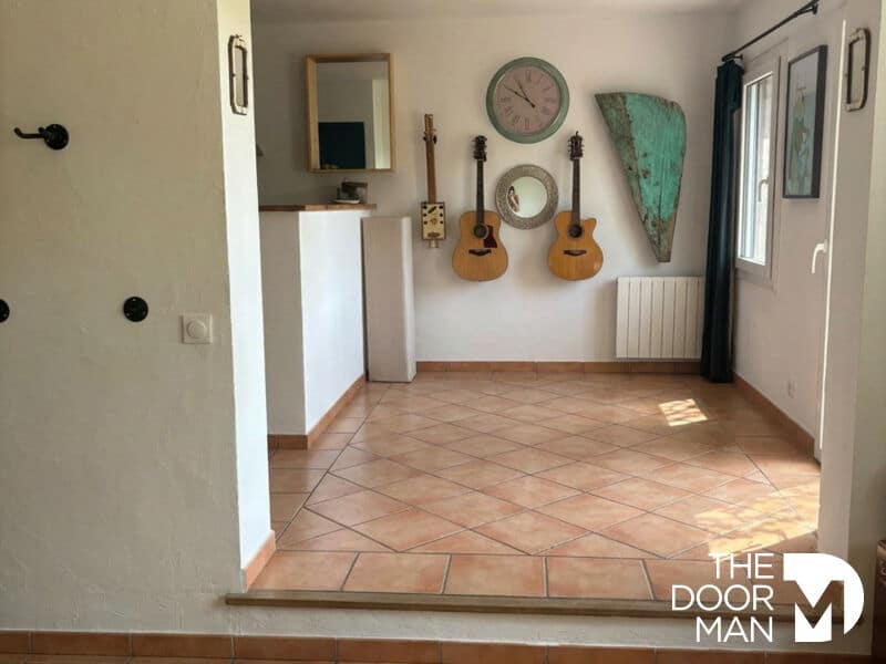 Intérieur d'une maison avec carrelage, deux guitares accrochées au mur et espace lumineux.