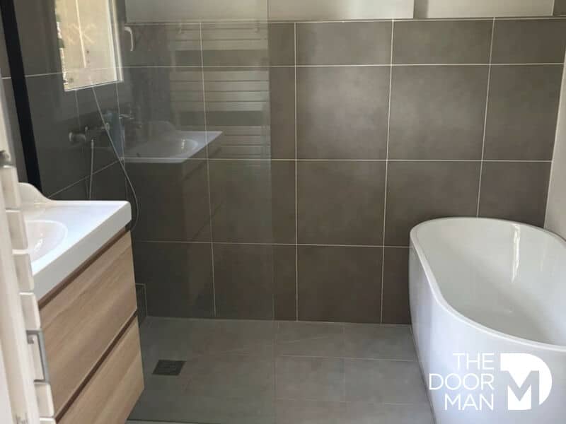 Salle de bain moderne avec douche et baignoire, carrelage gris, lumière naturelle