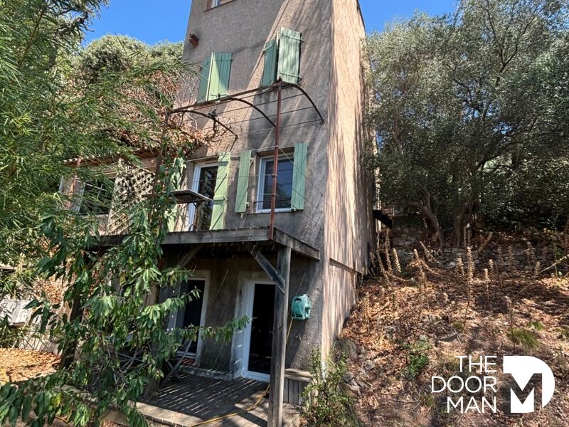 Maison atypique à Grimaud avec volets verts et terrasse, entourée de verdure.