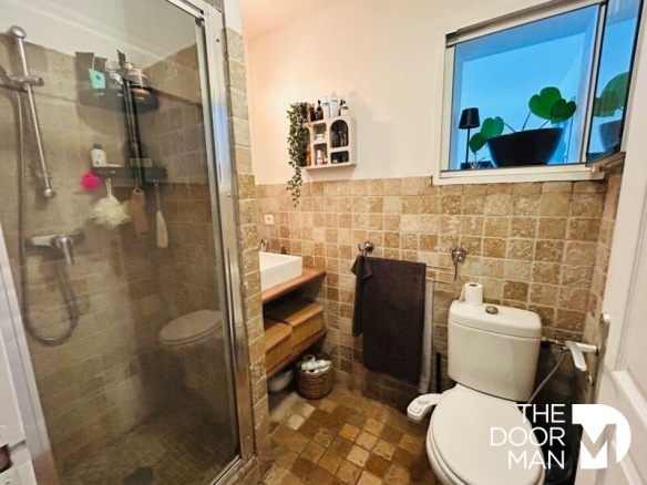 Salle de bain avec douche et toilettes, murs en carrelage beige, lavabo en bois.