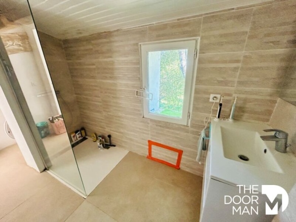 Salle de bain moderne avec douche et fenêtre, murs en carrelage clair.