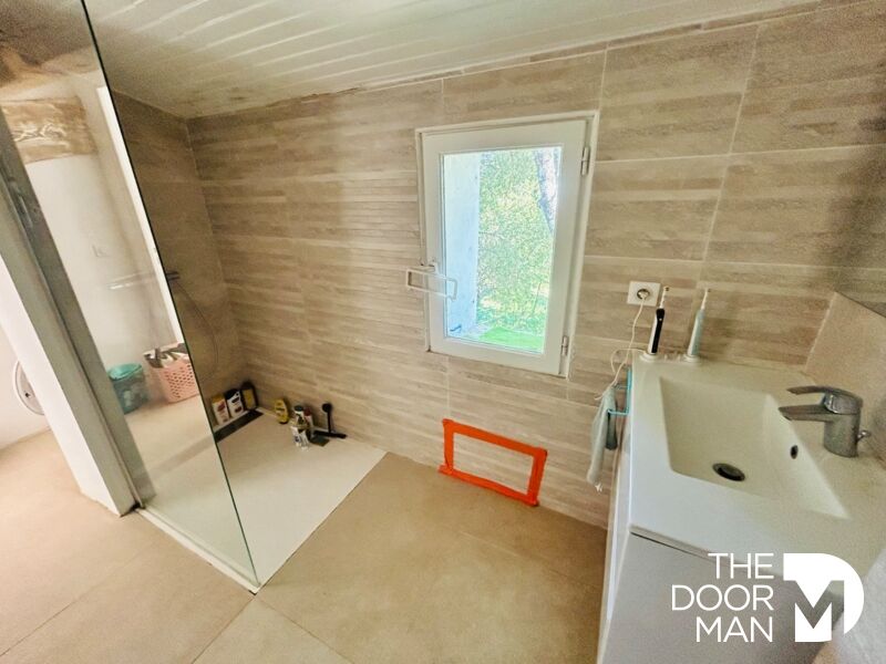Salle de bain rénovée Salle de bain moderne avec douche et fenêtre, murs en carrelage clair.