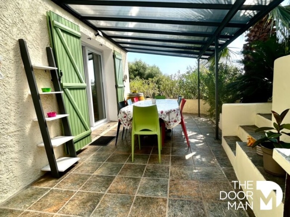 Terrace of a house with table and colorful chairs, surrounded by greenery in Le Lavandou.
