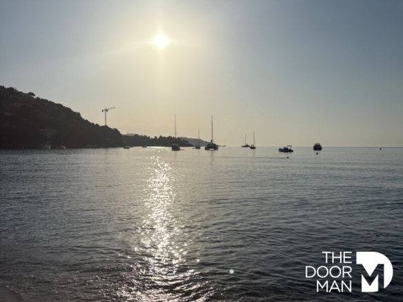 Vue de la plage de Saint Clair au Lavandou avec des bateaux au loin sous un ciel ensoleillé.