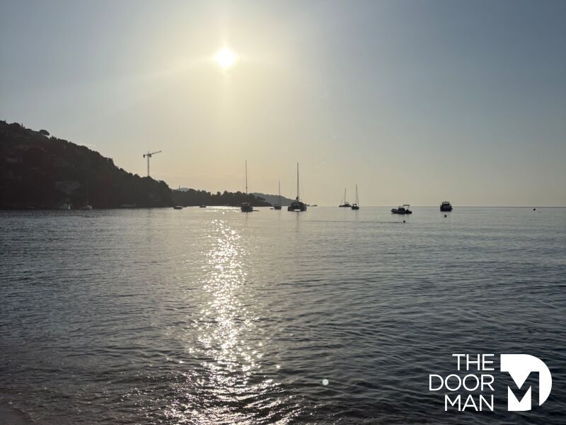 Plage de Saint Clair au Lavandou Vue de la plage de Saint Clair au Lavandou avec des bateaux au loin sous un ciel ensoleillé.