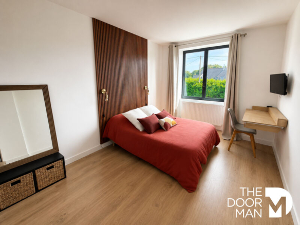 Room with red bed and wooden wall, desk and window overlooking the outside.