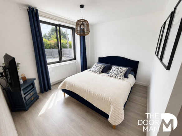 Room with double bed, television and windows letting in natural light.