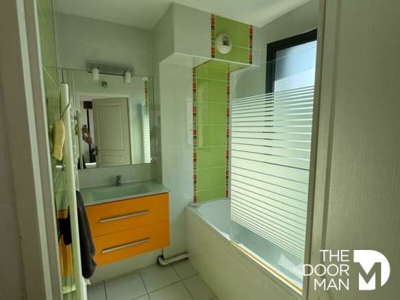 Modern bathroom with bathtub, orange furniture and tiled walls in Arcachon.
