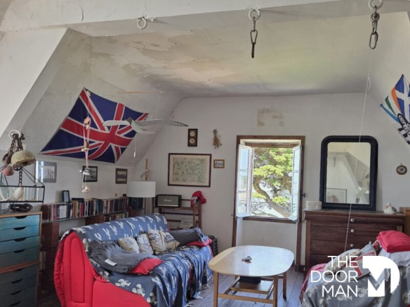 Intérieur d'un appartement avec un canapé rouge, des drapeaux et des livres, vue sur la plage de Sorlock.