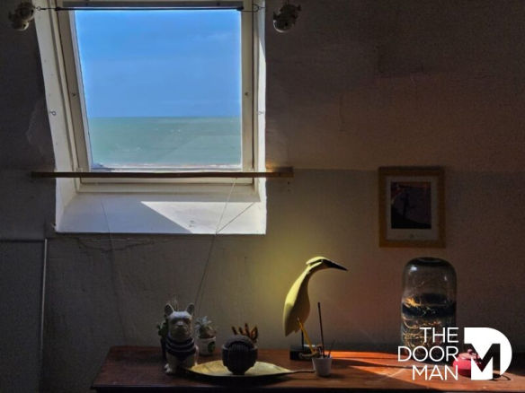 Vue depuis une fenêtre d'un appartement avec une décoration intérieure, montrant la mer au loin.