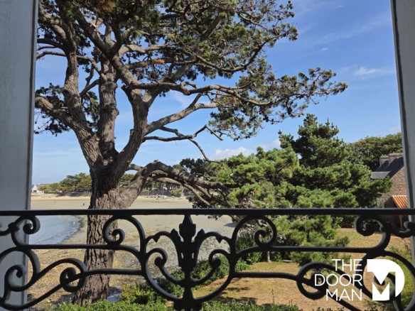 Vue depuis un balcon avec un arbre et la plage de Sorlock en arrière-plan.