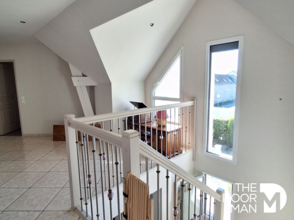Intérieur d'une maison moderne avec un escalier et des fenêtres lumineuses.