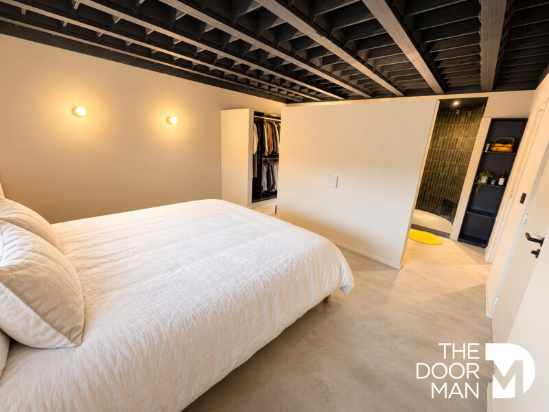 Chambre moderne avec lit double et salle de bain attenante, murs clairs et plafond noir.