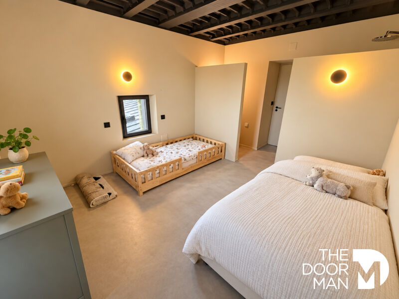 Chambre moderne avec lit double et lit d'enfant en bois, murs clairs et éclairage doux.