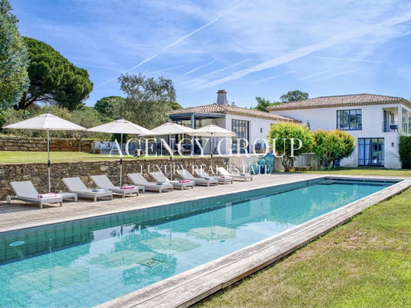 Luxurious villa with a rectangular pool, wooden deck, and white lounge chairs under umbrellas.