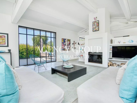 Bright, open-concept living room with white walls, large glass doors to a garden, and a black square coffee table between white sofas with turquoise cushions.