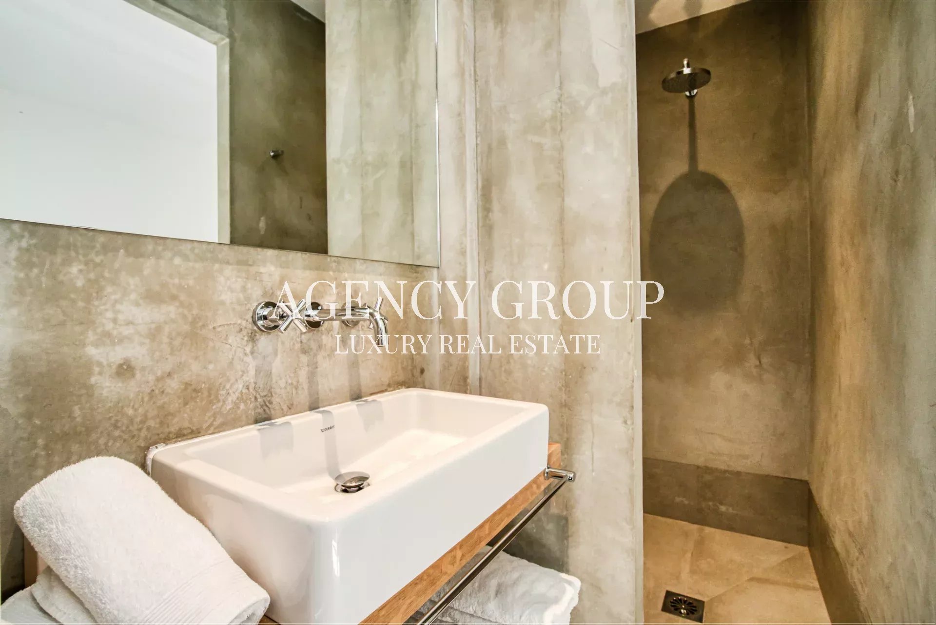 Luxurious concrete bathroom with a white rectangular sink, towel, and an open walk-in shower.