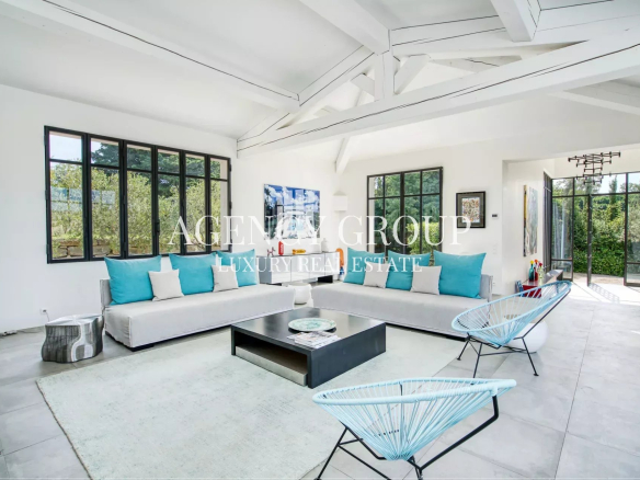 Bright modern living room with white walls and exposed beams, two white sofas with turquoise and white pillows, and a black coffee table.