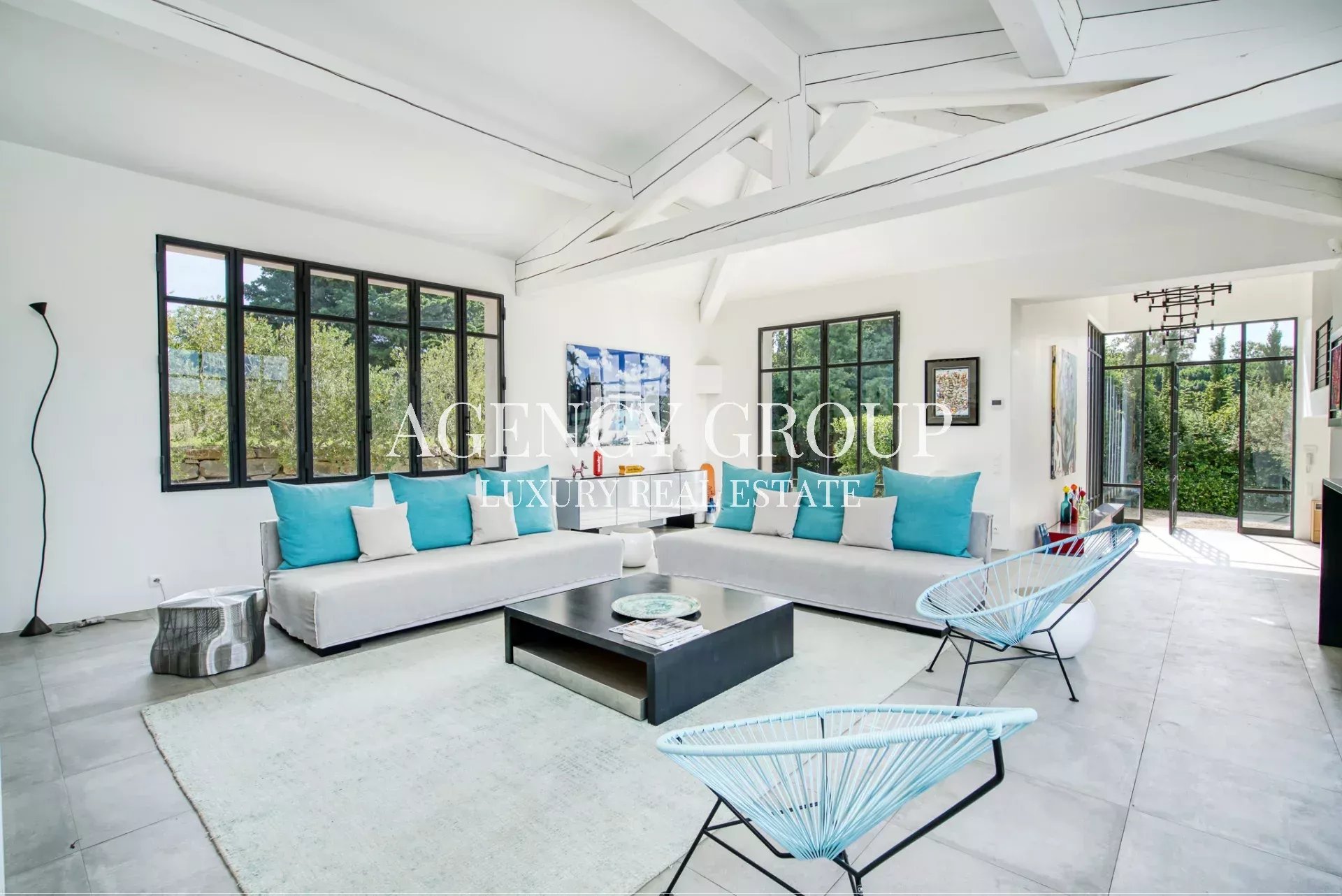 Bright modern living room with white walls and exposed beams, two white sofas with turquoise and white pillows, and a black coffee table.