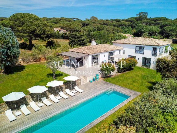 A white villa with tiled roofs, a rectangular turquoise pool, and a wooden deck with lounge chairs.