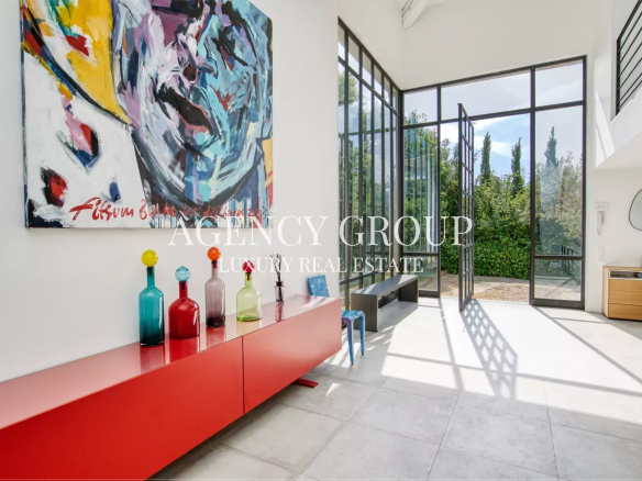 Bright, modern foyer with a large abstract painting on the wall and a red sideboard topped with colorful glass bottles, illuminated by natural light through tall glass doors to a garden.