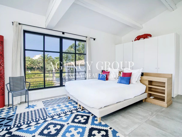 Bright modern bedroom with a large black-framed window, white bed, and blue geometric rug.