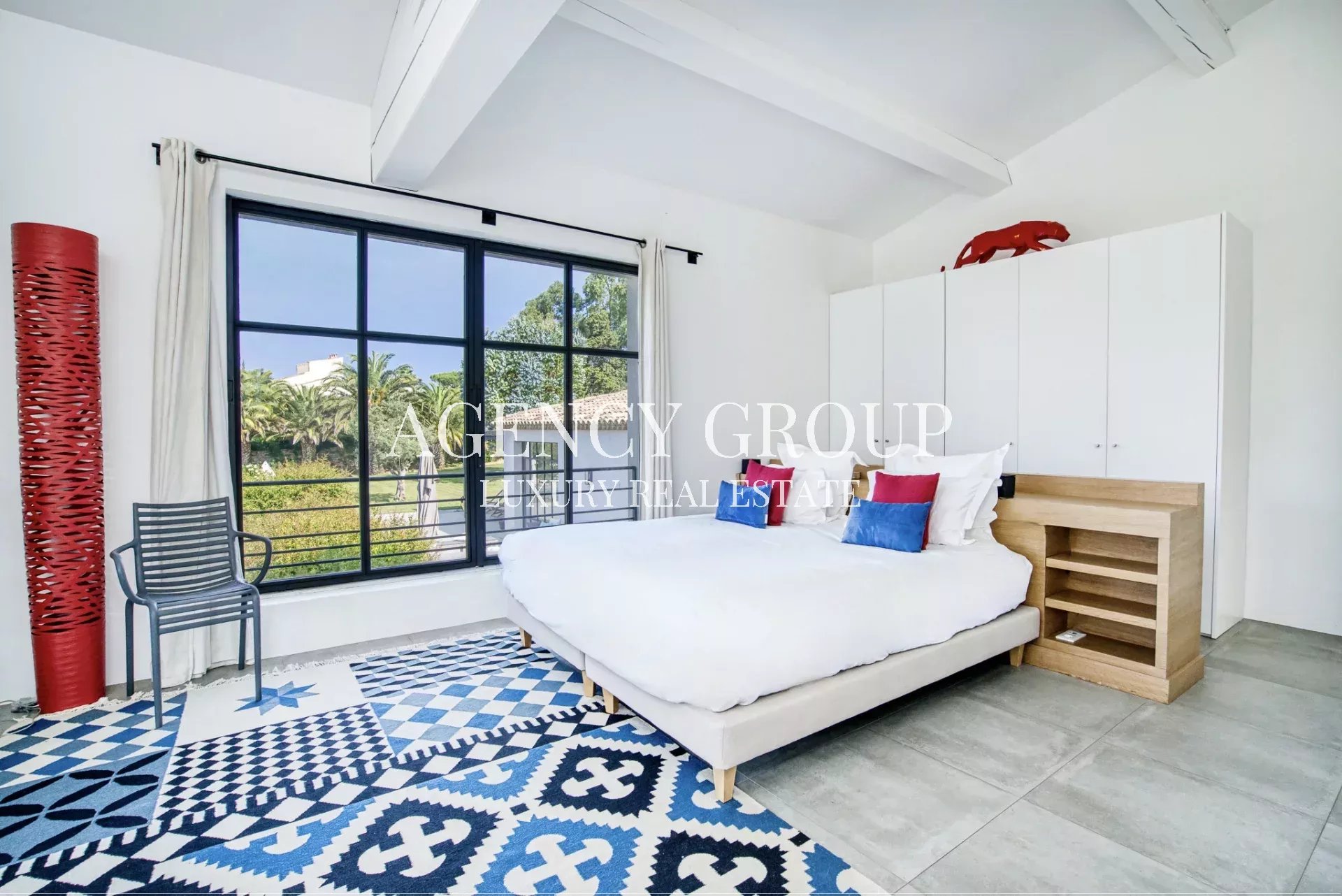 Bright modern bedroom with a large black-framed window, white bed, and blue geometric rug.