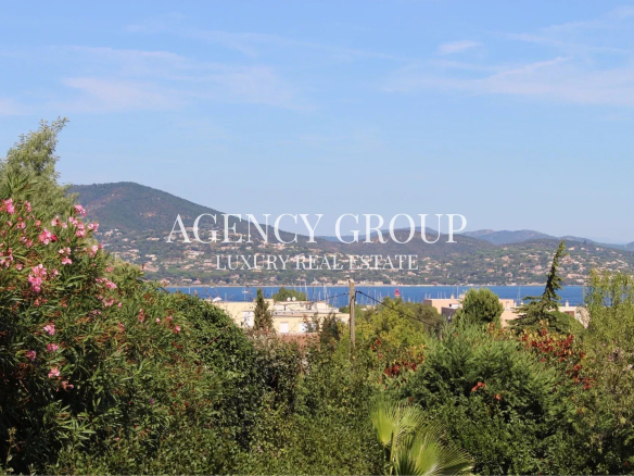 Coastal landscape with hills, blue sea, and green foreground; white overlay text reads 'AGENCY GROUP LUXURY REAL ESTATE'.