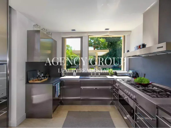 Contemporary stainless steel kitchen with double ovens, a gas range, and a window overlooking greenery above the sink area (watermark text present).