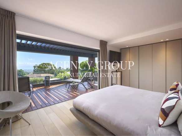 Luxurious bedroom with a sliding glass door opening to a wooden balcony, overlooking trees and distant city views