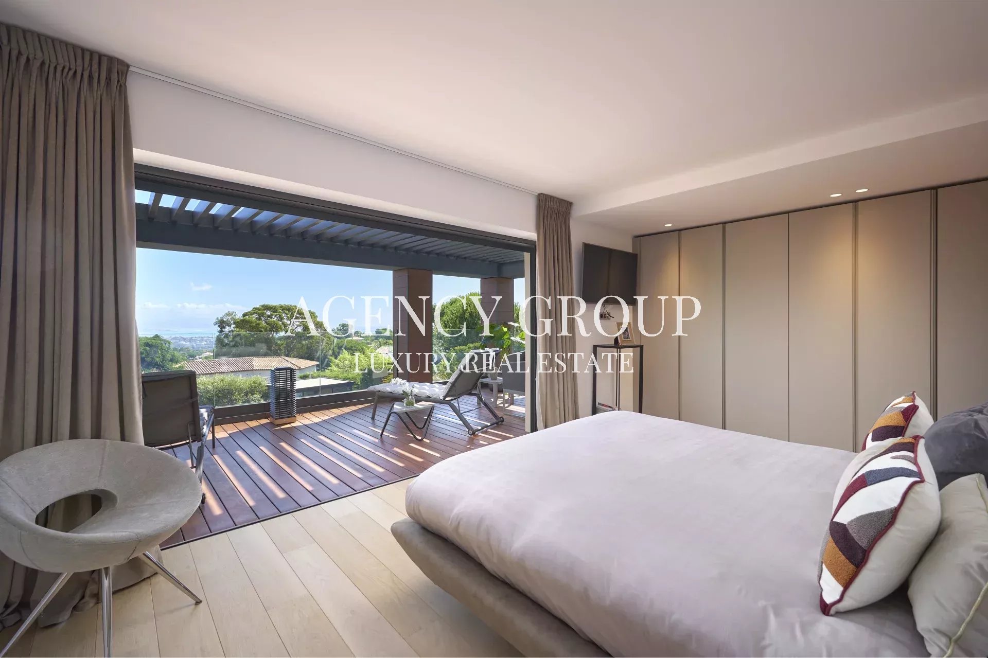 Luxurious bedroom with a sliding glass door opening to a wooden balcony, overlooking trees and distant city views