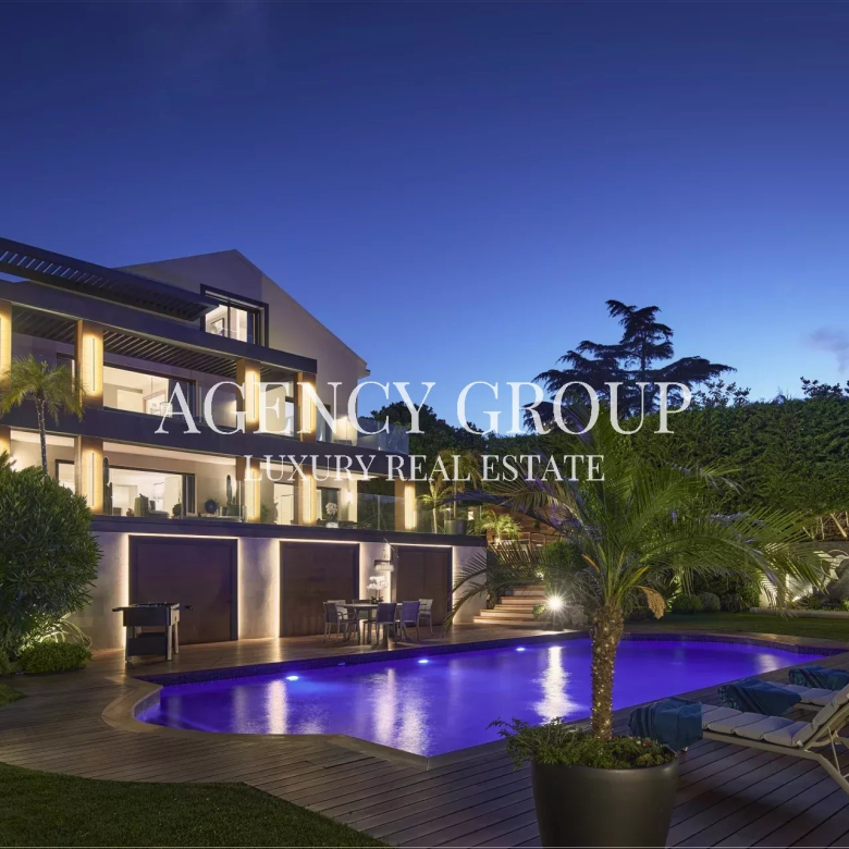 Modern luxury villa at dusk with illuminated exterior, blue-lit pool, and poolside lounge chairs.