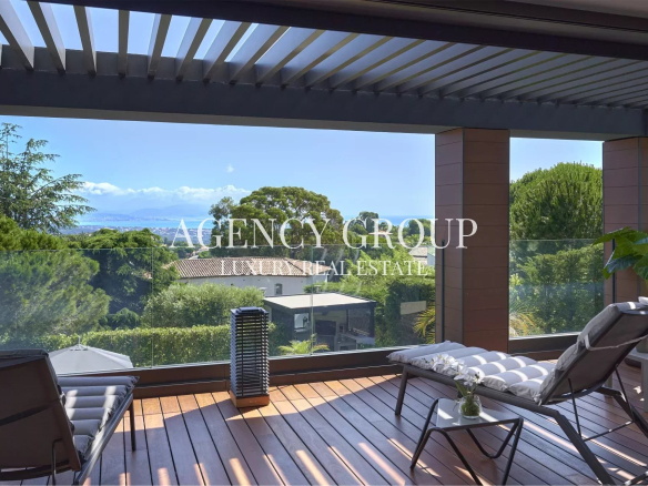 Modern balcony with wooden decking and glass railing overlooking lush trees and distant sea. (watermark: AGENCY GROUP REAL ESTATE)