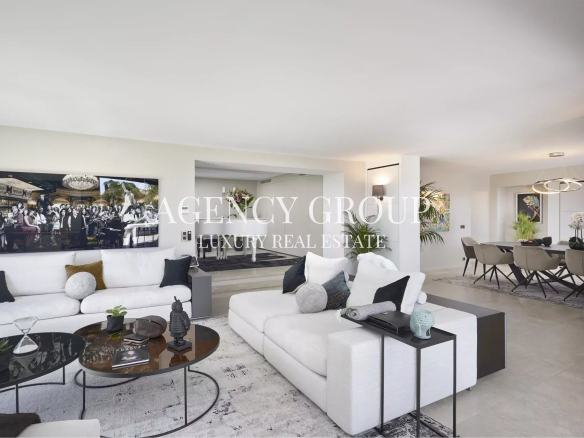 Open-plan living room with white sectional sofas, round glass coffee tables, and neutral decor; dining area visible in the background.