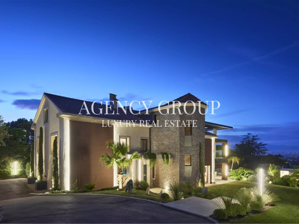 Twilight exterior of a modern luxury house with landscaped grounds and a large 'Agency Group Luxury Real Estate' logo across the facade.