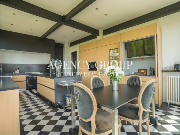 Open-plan kitchen with light wood cabinets, black countertops, built-in oven, and a dining table with four upholstered chairs on a black-and-white checkered floor.