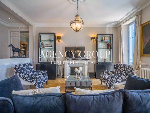 Elegant living room with a central glass coffee table, navy sofas, and patterned chairs facing a fireplace and built-in display cabinets.