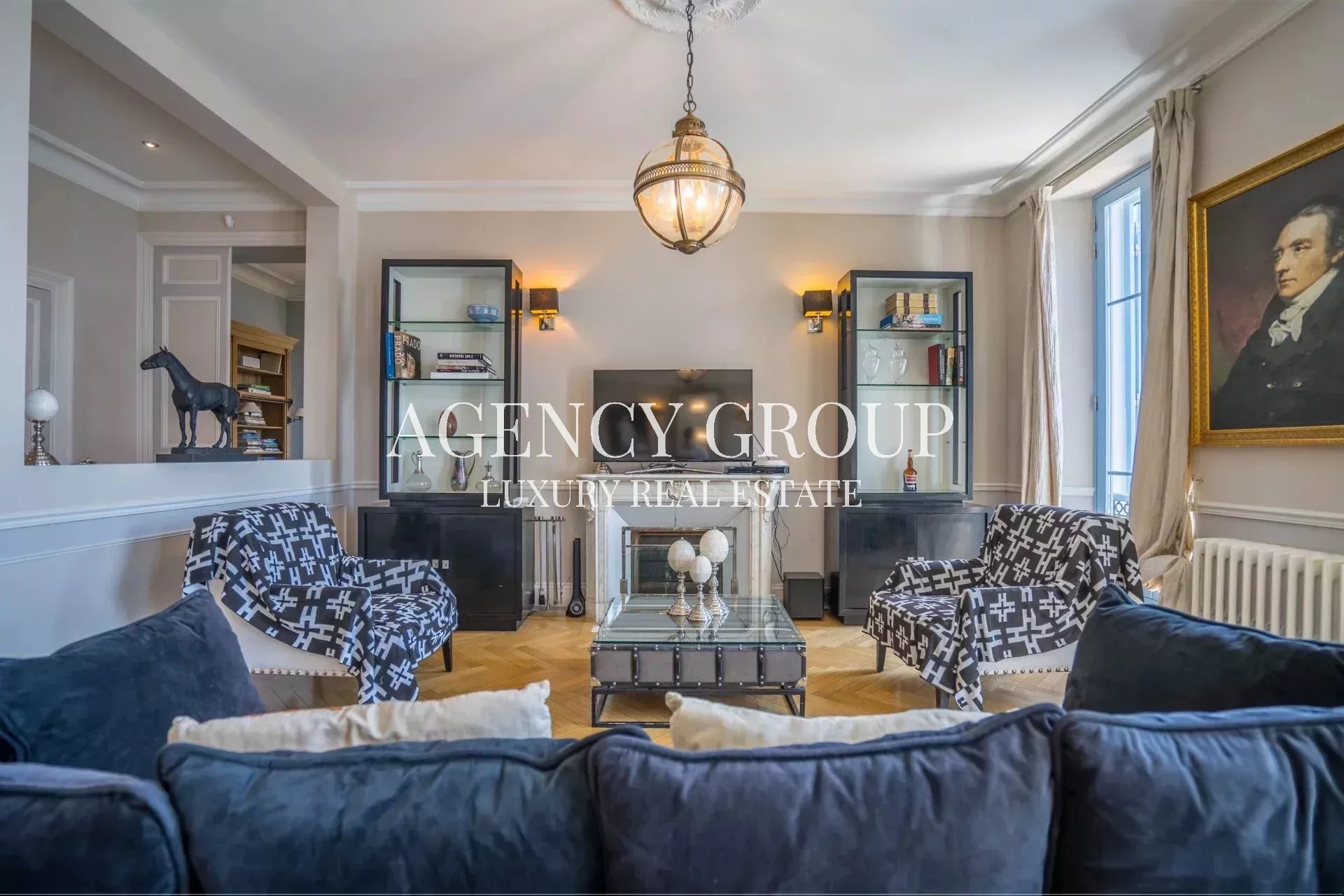 Elegant living room with a central glass coffee table, navy sofas, and patterned chairs facing a fireplace and built-in display cabinets.