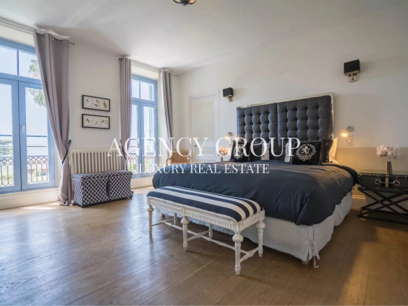 Luxurious bedroom with a tufted black headboard, navy bedding, and a striped bench at the foot of the bed, illuminated by bedside lamps.