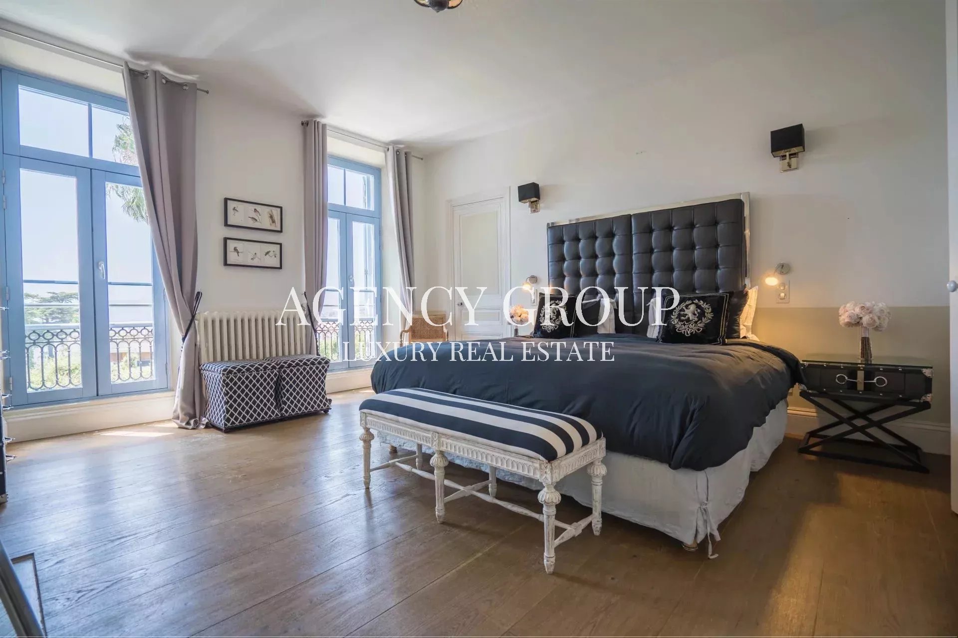 Luxurious bedroom with a tufted black headboard, navy bedding, and a striped bench at the foot of the bed, illuminated by bedside lamps.