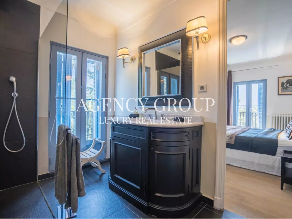 Luxurious en-suite bathroom with a black curved vanity, marble countertop, and wall sconces, connected to a bedroom with balcony doors.