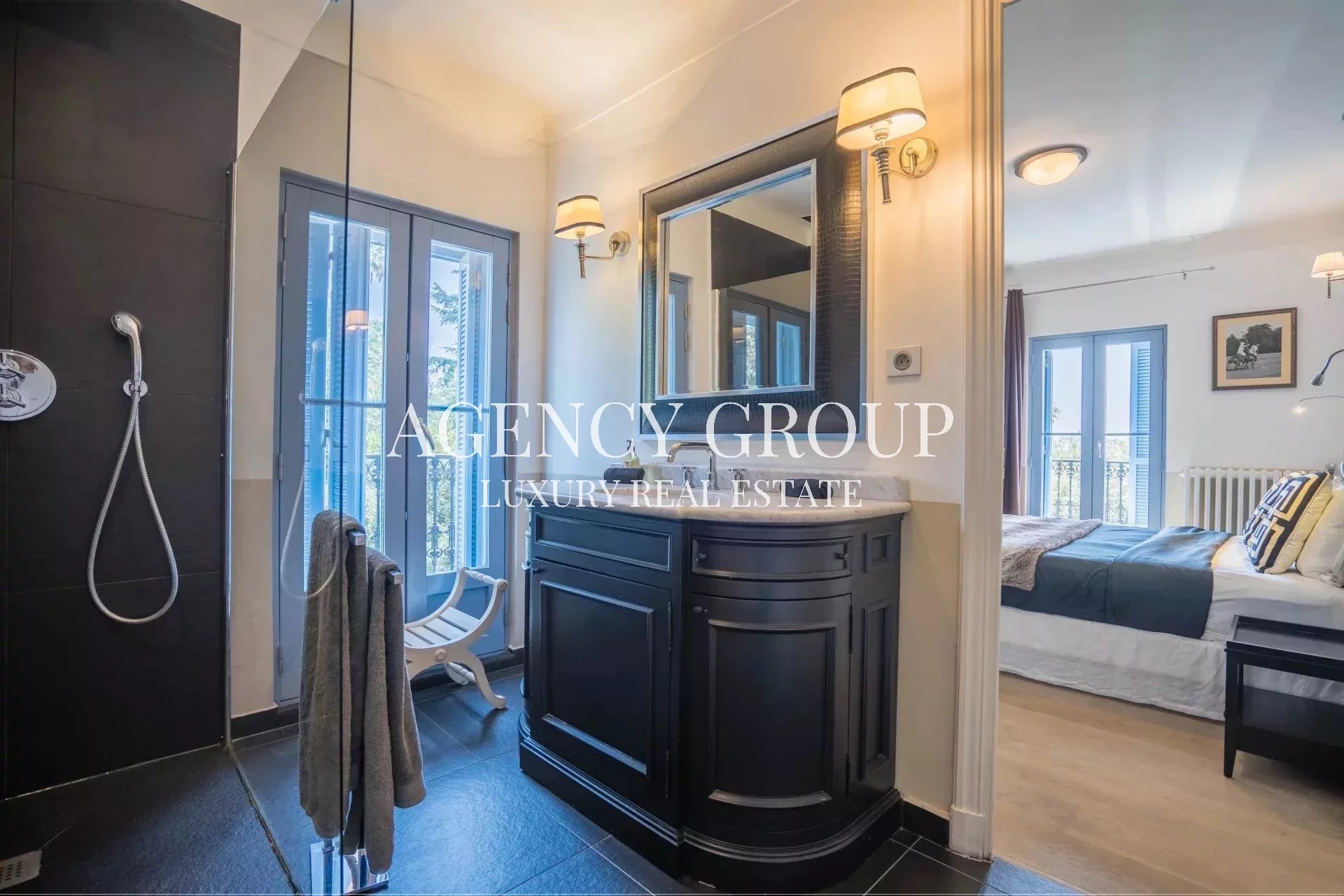 Luxurious en-suite bathroom with a black curved vanity, marble countertop, and wall sconces, connected to a bedroom with balcony doors.