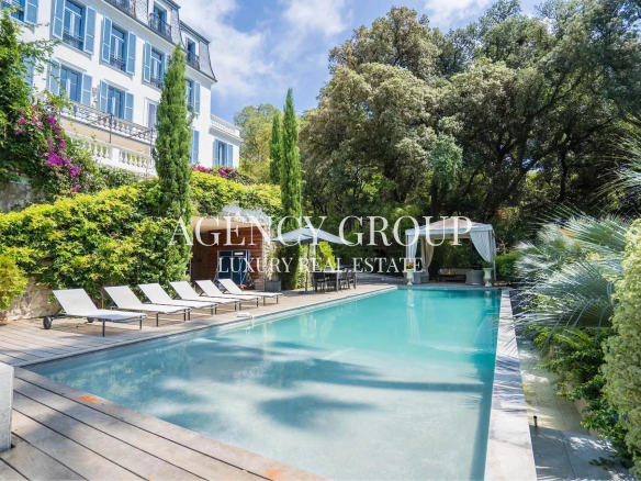 Poolside view of a luxury villa with a wooden deck, white lounge chairs, and lush greenery surrounding the area