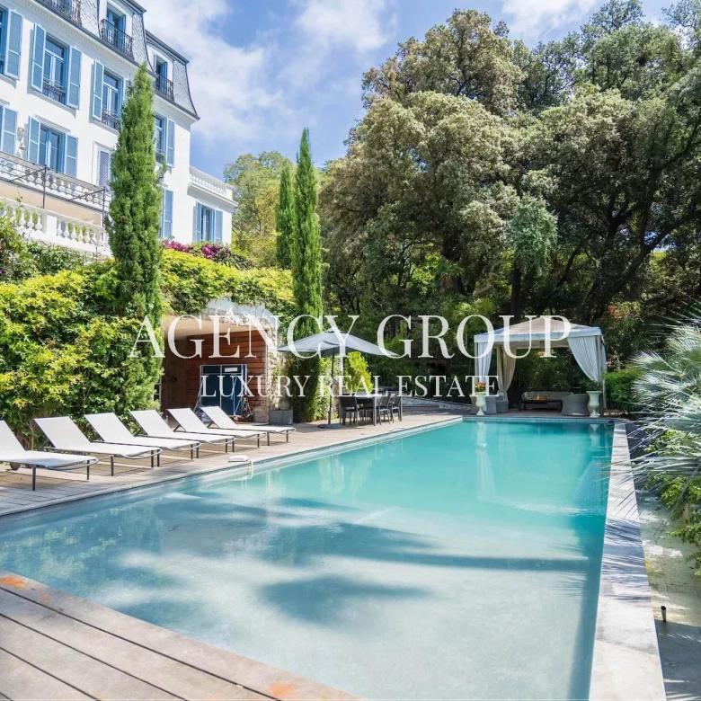 Poolside view of a luxury villa with a wooden deck, white lounge chairs, and lush greenery surrounding the area