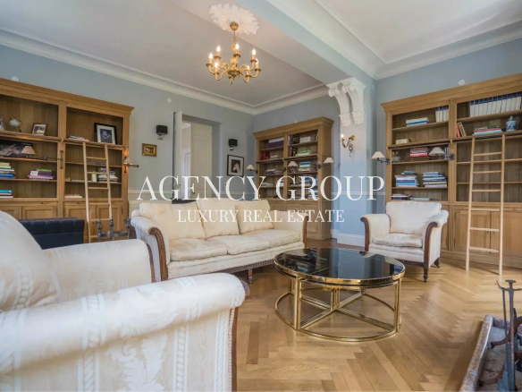 Elegant living room in a luxury home: blue walls, cream sofas, wooden bookcases with ladders, and a gold glass coffee table under a chandelier.