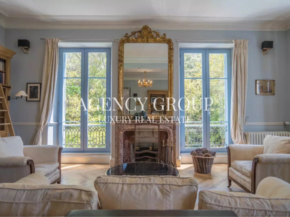 Elegant living room with blue-trimmed windows, cream sofas, and a gold ornate mirror above a marble fireplace.
