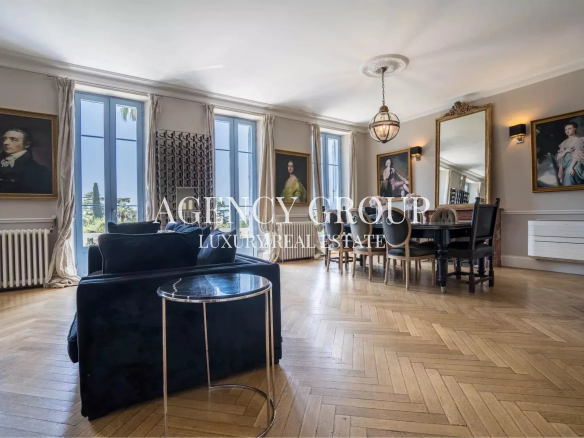 Luxurious living and dining room with a blue velvet sofa, round marble side table, tall windows, and a large dining table.